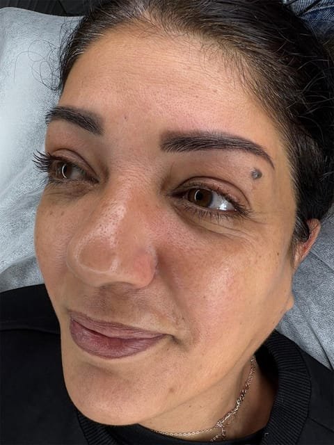 מטופלת מחייכת לאחר איפור קבוע גבות, גוון כהה ומוגדר